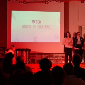 Drei Schülerinnen, die auf der Bühne stehen, eingetaucht in rotes Licht.